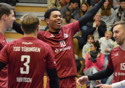 Ein jubelndes Volleyball-Team der TSG Tübingen in weinroten Trikots. Die Spieler lachen und feiern einen Punktgewinn in einer gut besuchten Sporthalle.