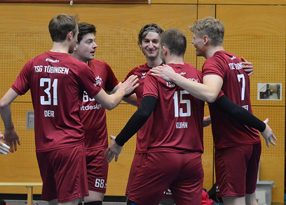 Fünf Handballspieler in roten Trikots umarmen sich in der Halle nach einem Treffer