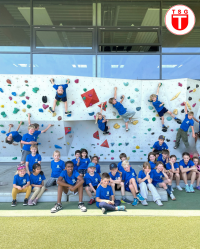 Gruppenfoto einer Jugend-Klettergruppe vor einer Kletterwand mit Kindern und Betreuern in blauen Shirts im Innenraum