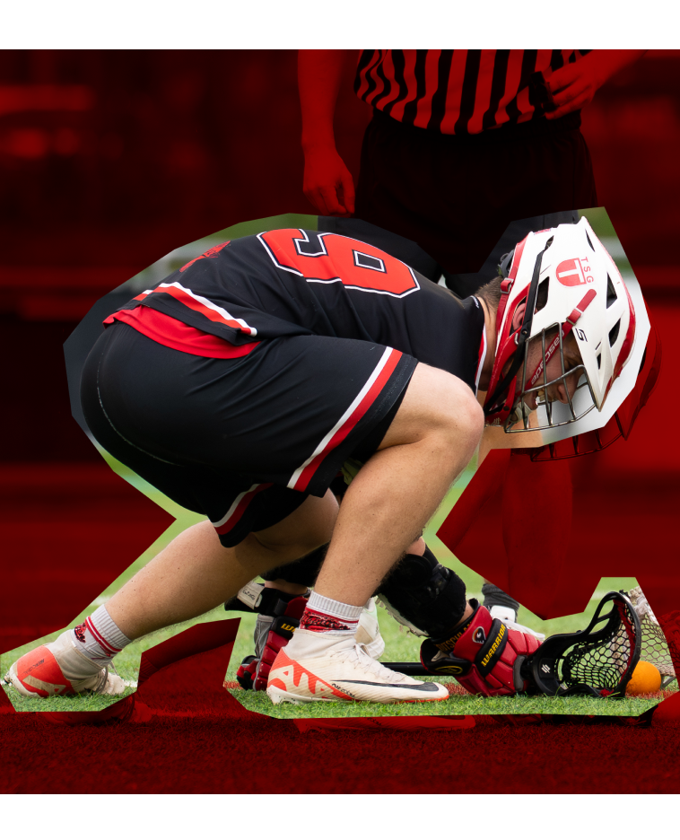 Ein Lacrosse-Spieler kniet auf dem Boden, trägt eine Helm- und Schutzausrüstung und hält den Schläger in der Nähe eines Balls auf dem Spielfeld.